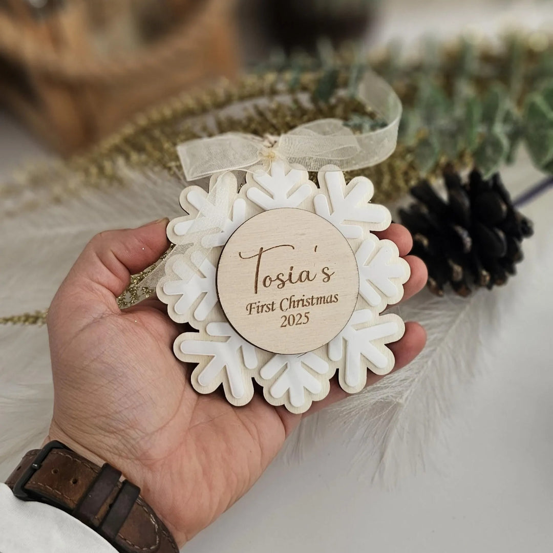 A person's hand holding a wooden ornament with a snowflake design and a personalized message.