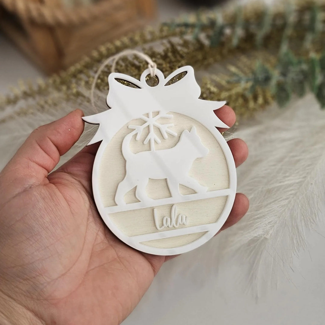 A hand holding a white ornament with a cat silhouette and the word "lala" written on it.
