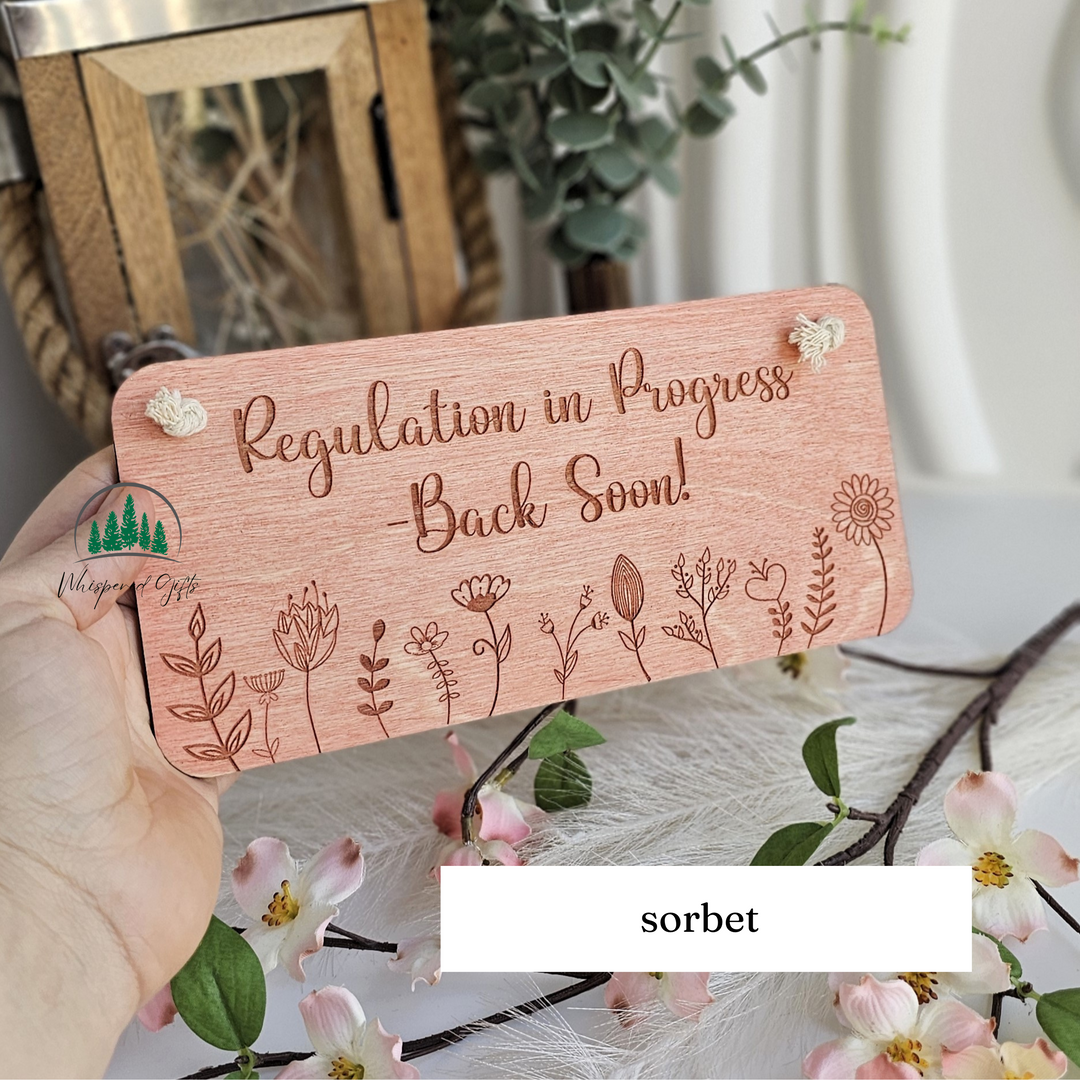 A wooden sign with the text "Regulation in Progress - Back Soon!" is being held in front of a floral arrangement.