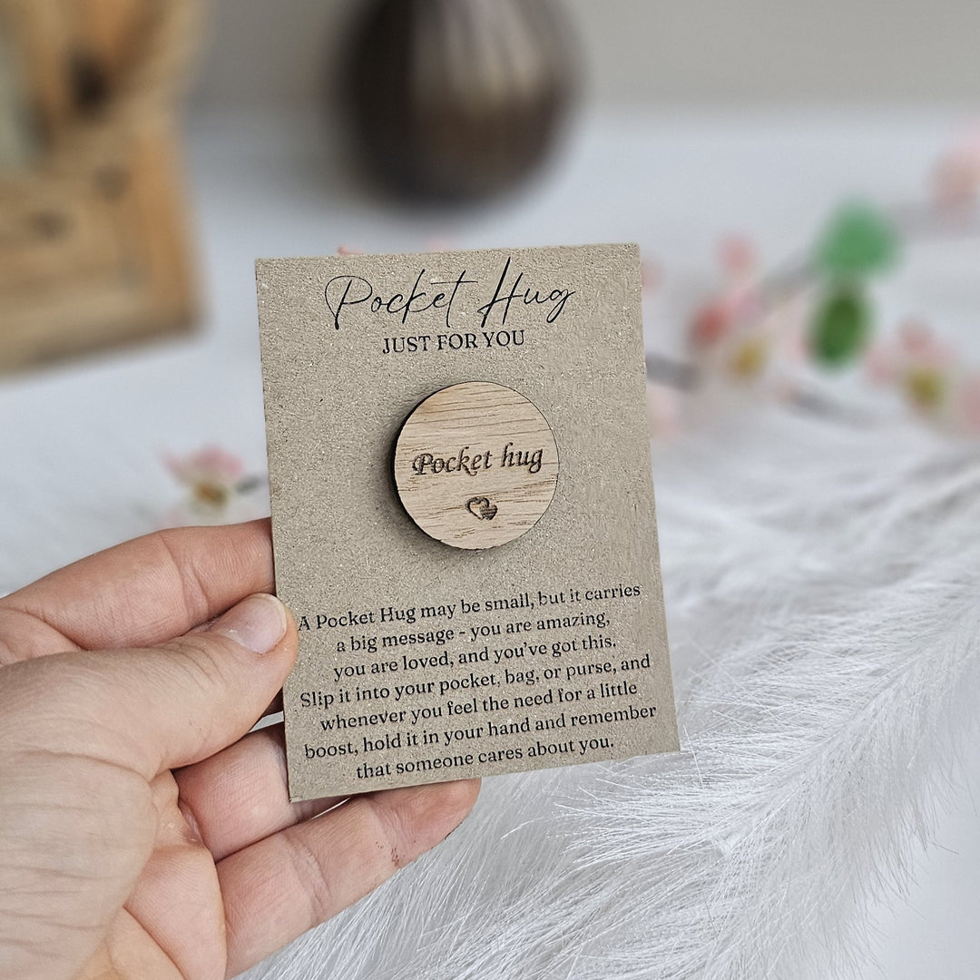 A hand holding a small wooden "Pocket Hug" magnet with a message about the importance of a heartfelt message.