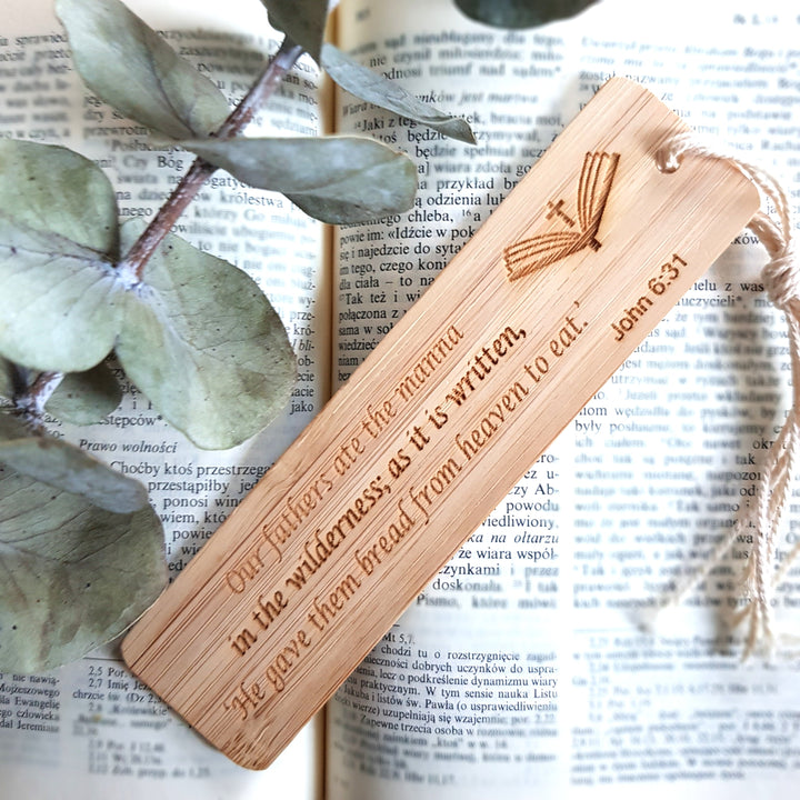 A wooden bookmark with a Bible verse engraved on it, resting on top of an open book with text visible.