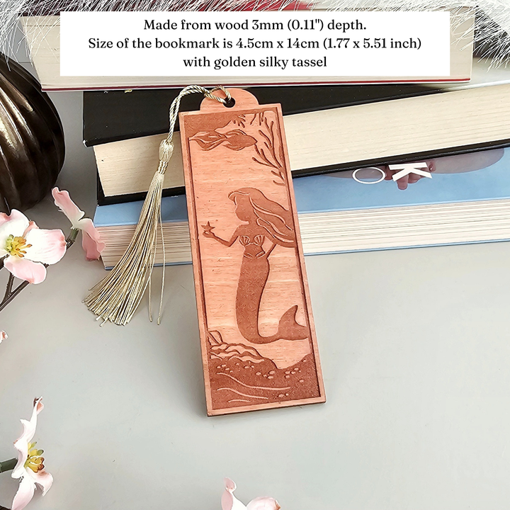 A wooden bookmark with a mermaid design, placed on top of a stack of books.