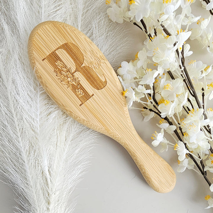 A wooden brush with a letter "R" engraved on it, surrounded by white flowers and feathers.