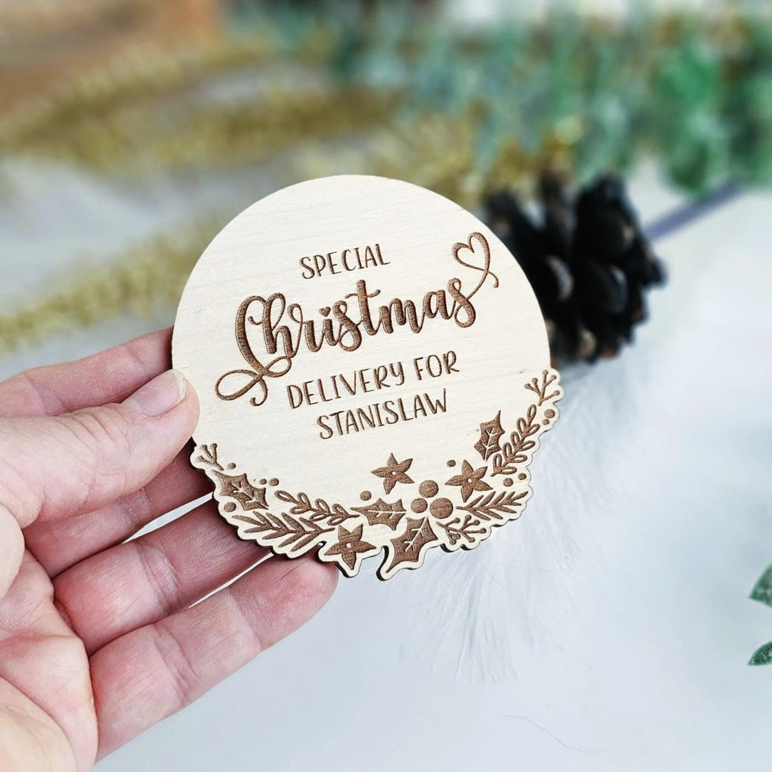 A hand holding a wooden coaster with the text "Special Christmas Delivery for Stanislaw" engraved on it.