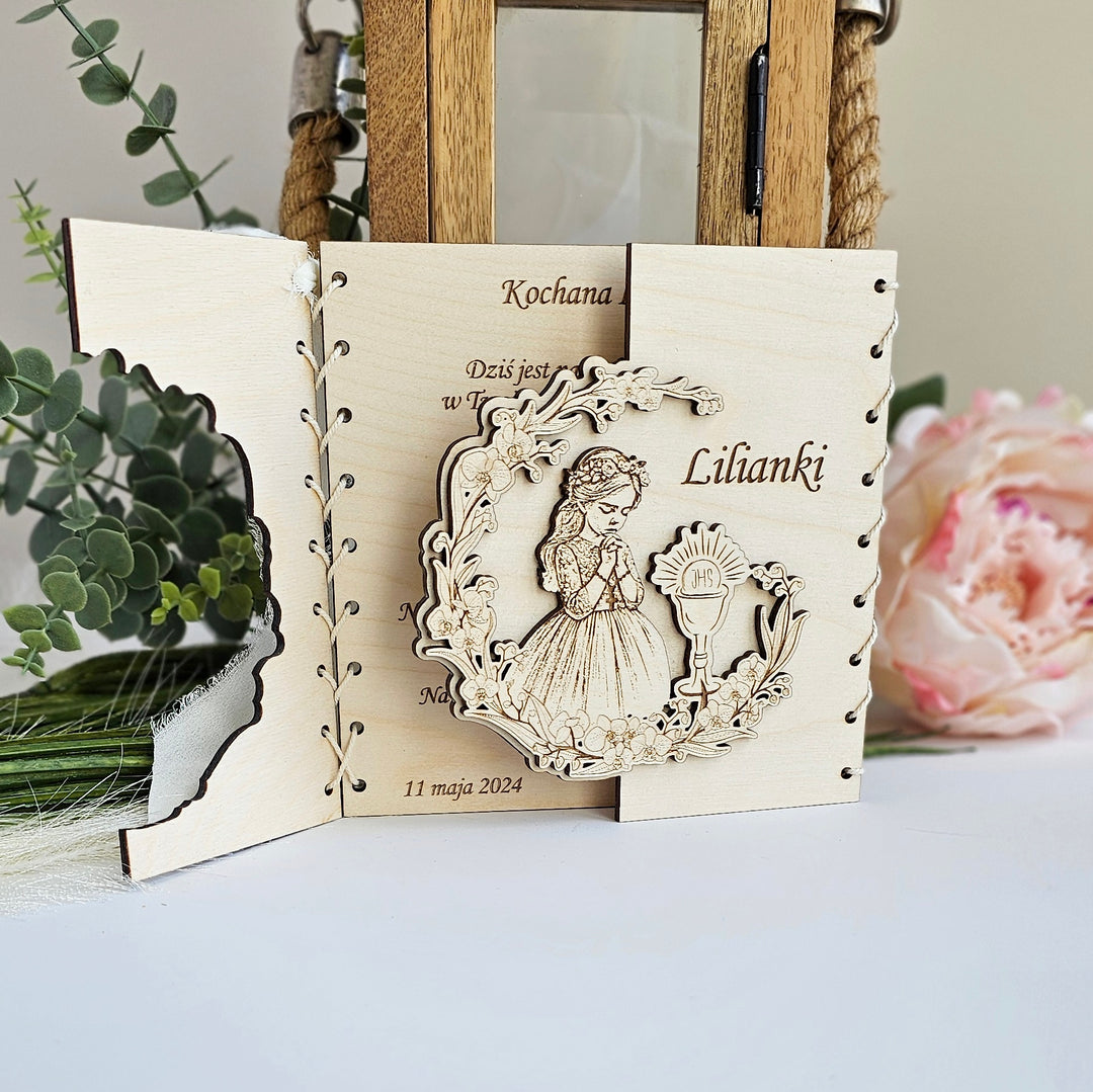 A wooden card with a carved design featuring a girl and a flower, placed on a table with a pink flower in the background.