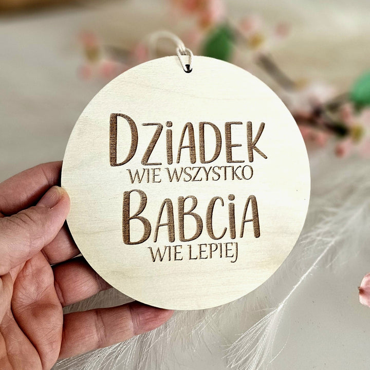 A hand holding a wooden sign with text in Polish.