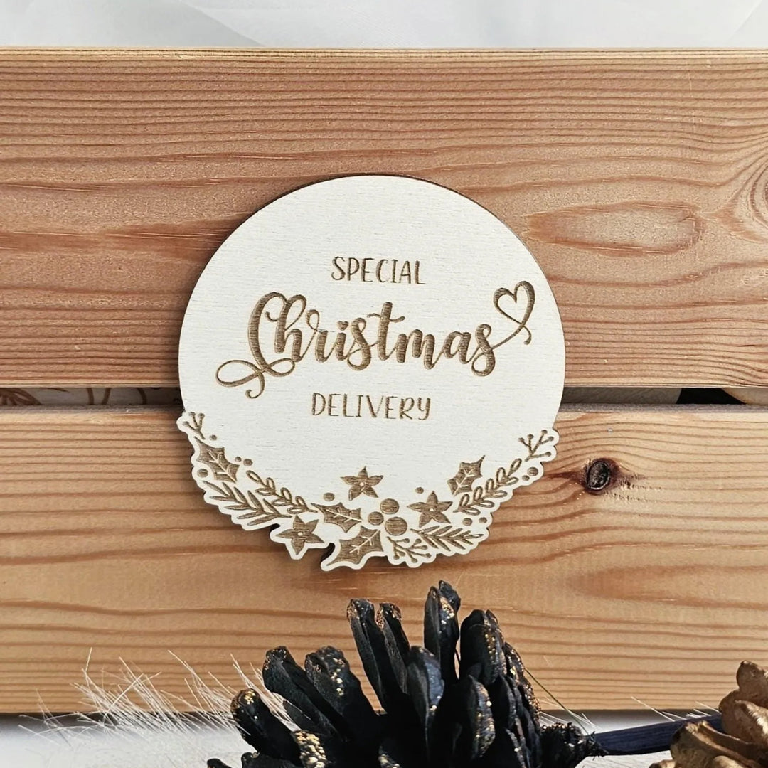 A wooden sign with the text "SPECIAL Christmas delivery" is displayed on a wooden surface, with pine cones and other decorative items in the foreground.