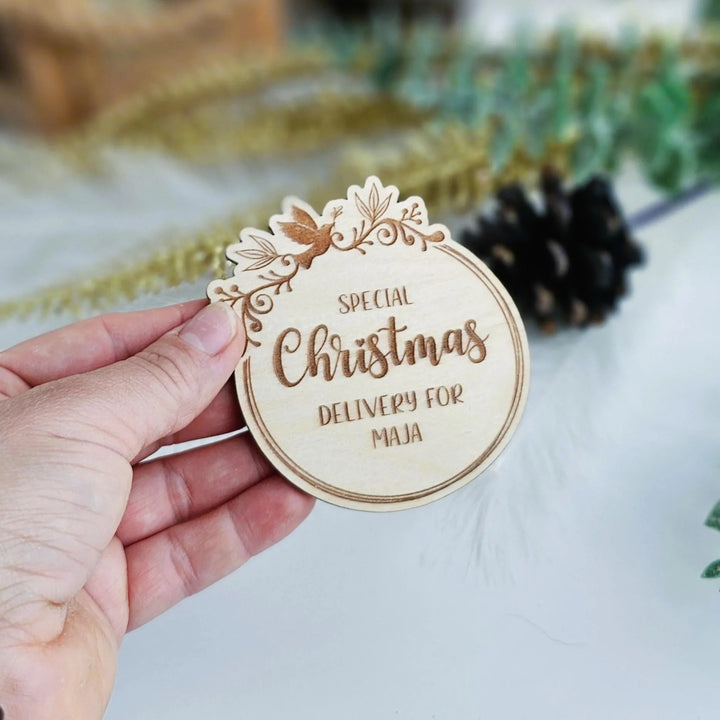 A hand holding a wooden Christmas card with the text "Special Christmas Delivery for Maja" on it.