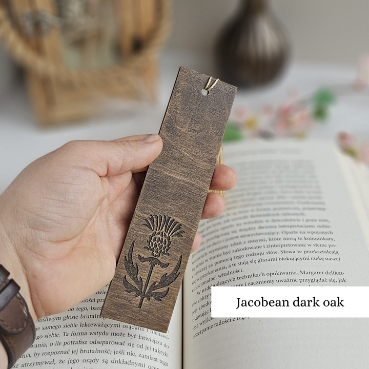 A hand holding a wooden bookmark with a design on it, resting on an open book.