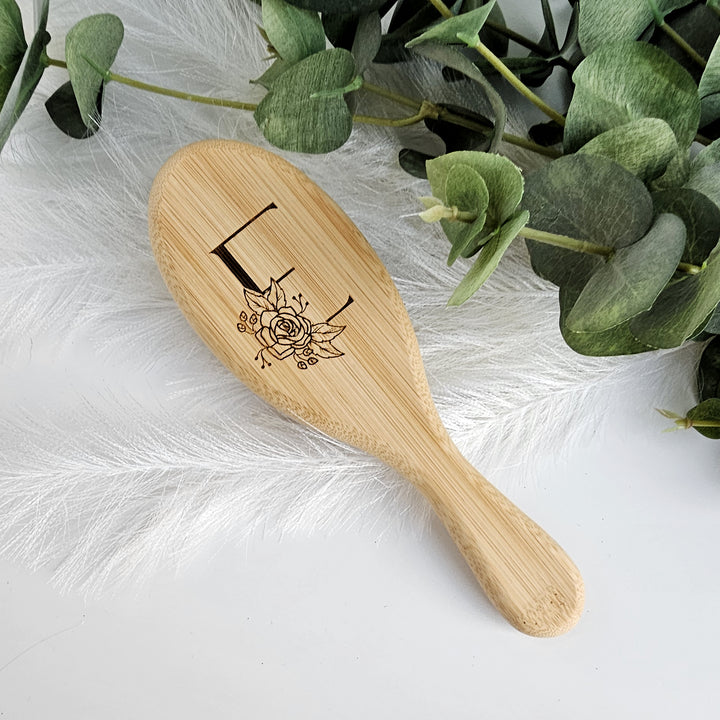 A wooden brush with a floral design on it, placed on a white surface next to some greenery.