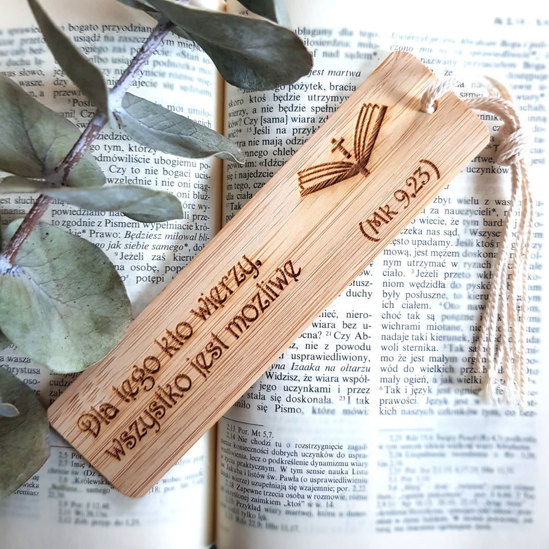 A wooden bookmark with a cross and text engraved on it, resting on top of an open book with text visible.
