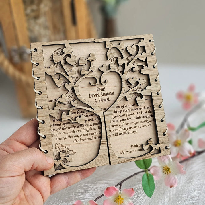 A hand is holding a wooden box with a tree-like design on it, surrounded by flowers and greenery.