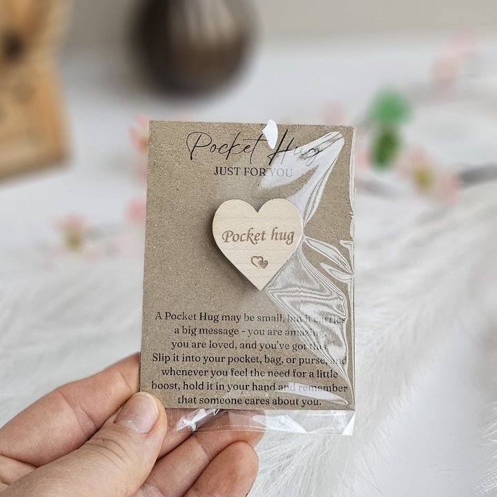 A person's hand holding a wooden heart-shaped object with text on it.