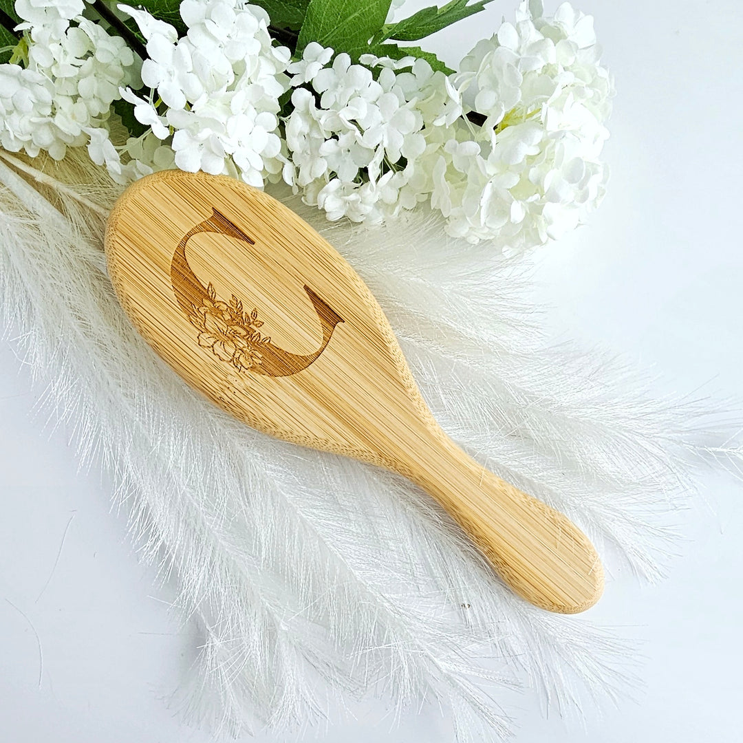 A wooden brush with a floral design rests on a white background, surrounded by white flowers and feathers.