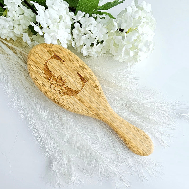 A wooden brush with a floral design rests on a white background, surrounded by white flowers and feathers.