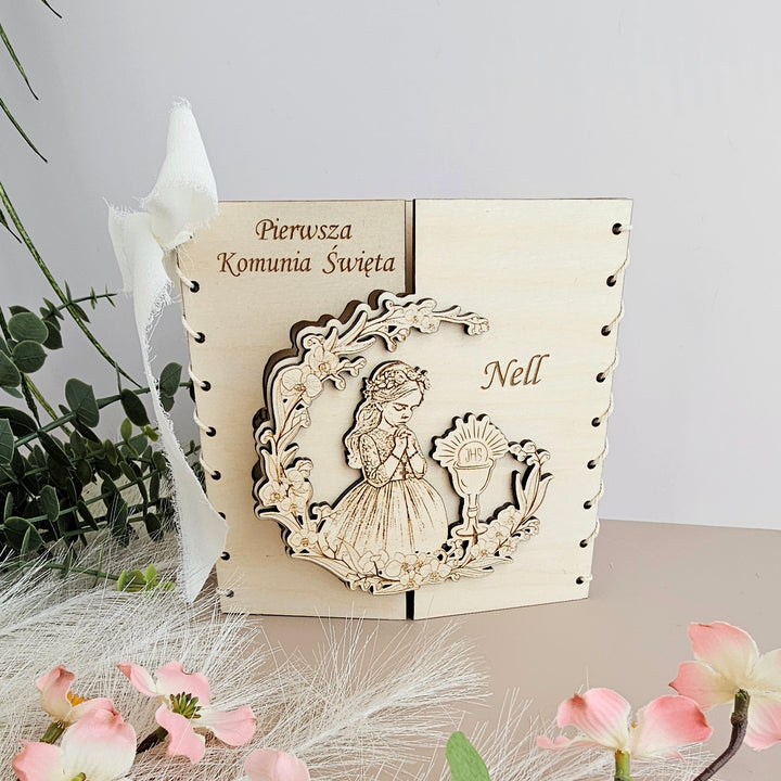 A wooden box with a carved image of a young girl, surrounded by flowers and greenery, with the names 'Pierwsza Komunia Swieta' and 'Neill' carved on it.