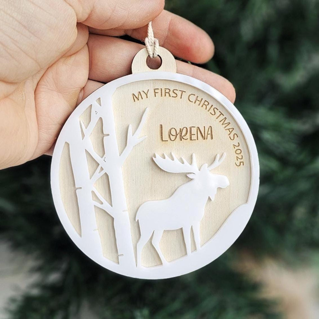 Baby’s First Christmas ornament with woodland moose design hanging on tree.