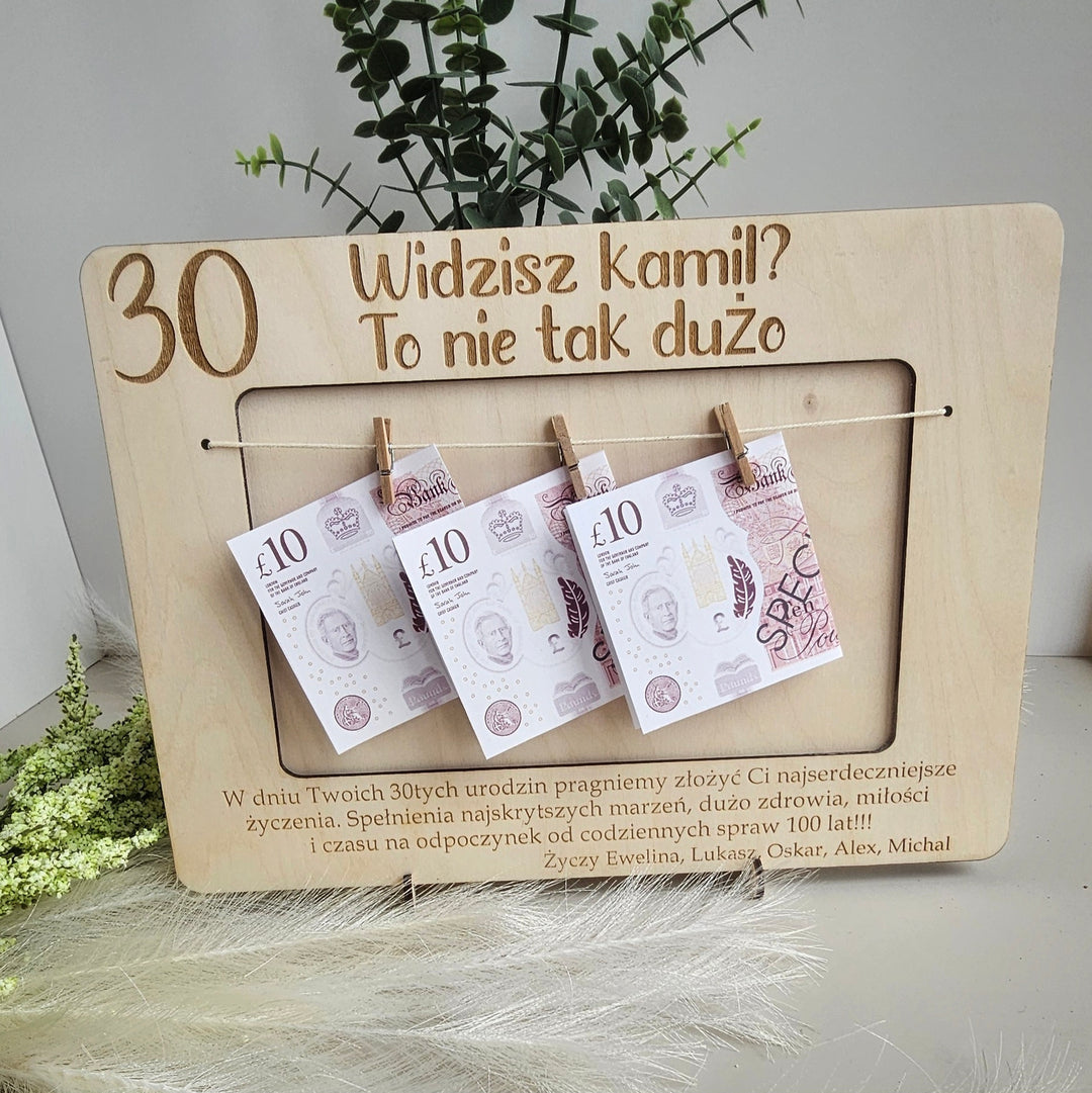 A wooden frame with three £10 banknotes hanging from it, placed on a white surface.
