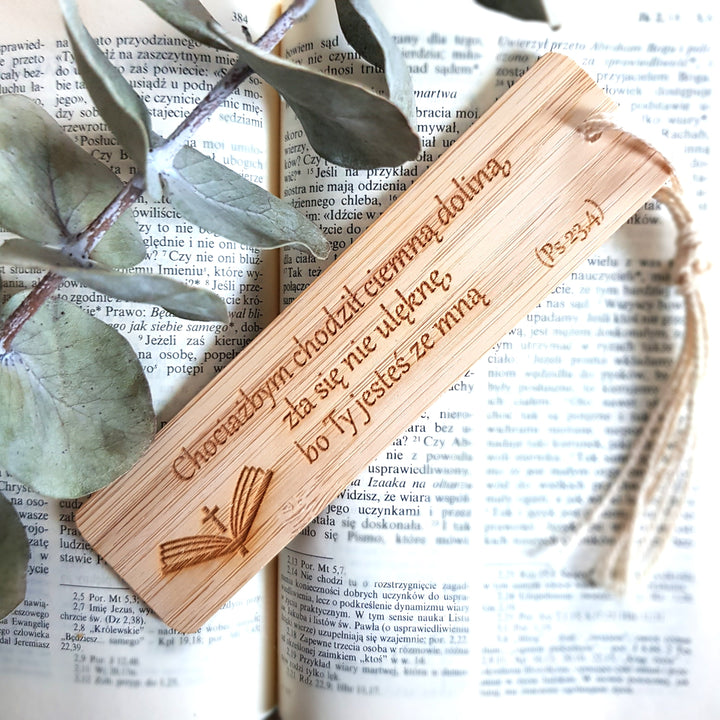 A wooden bookmark with a Bible verse engraved on it, resting on top of an open book with text visible.