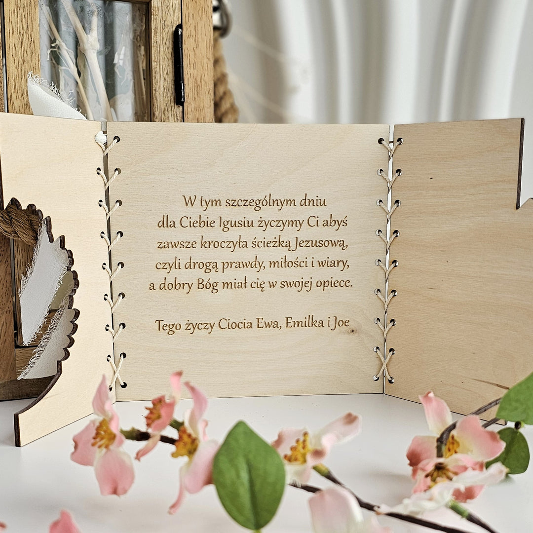 a wooden card with a message written in Polish, placed on a table with pink flowers in the foreground.