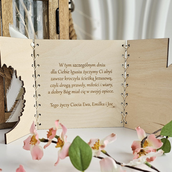 a wooden card with a message written in Polish, placed on a table with pink flowers in the foreground.