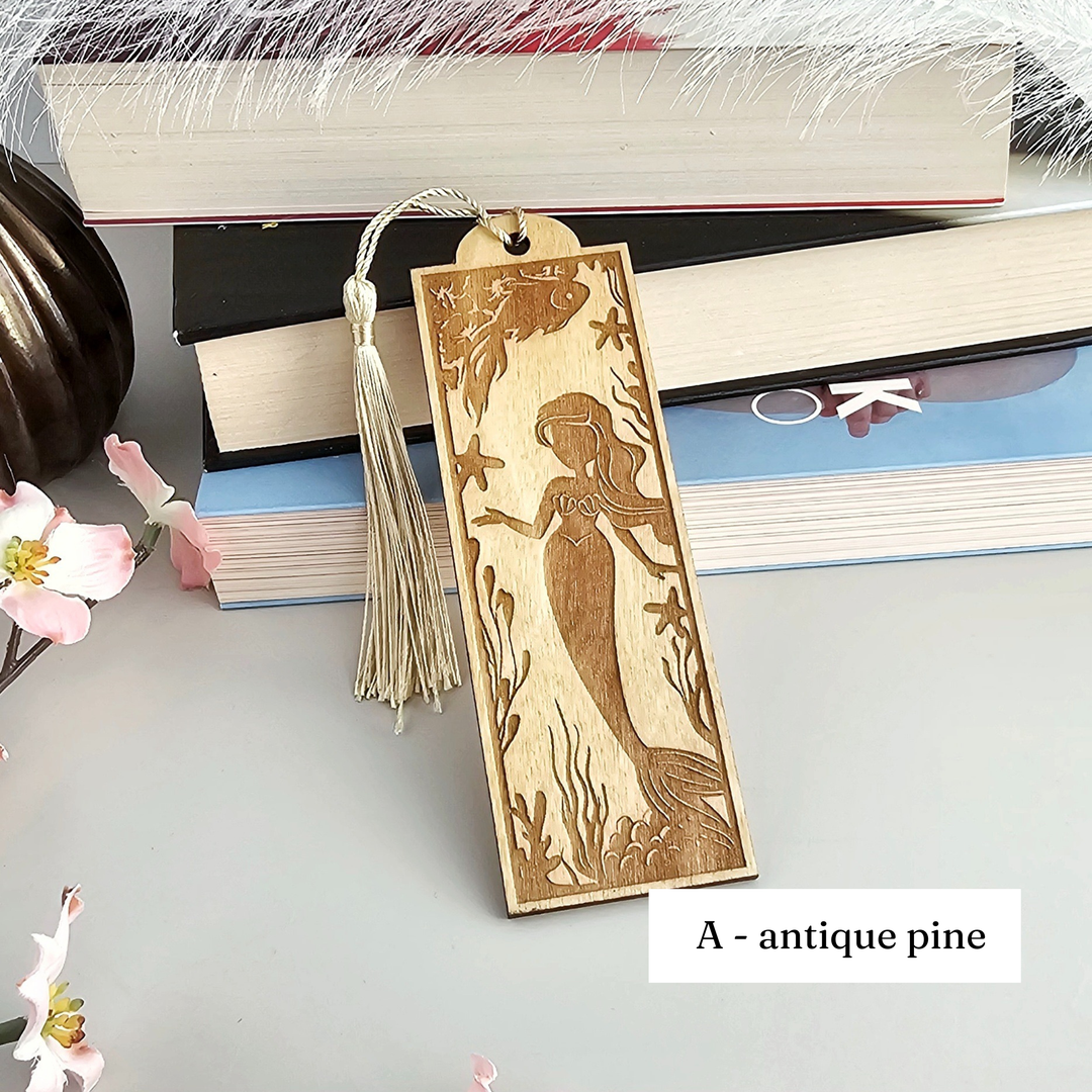A wooden bookmark with a mermaid design, placed on top of a stack of books.