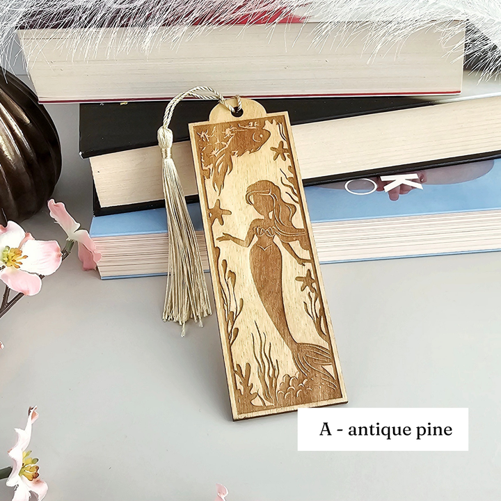 A wooden bookmark with a mermaid design, placed on top of a stack of books.