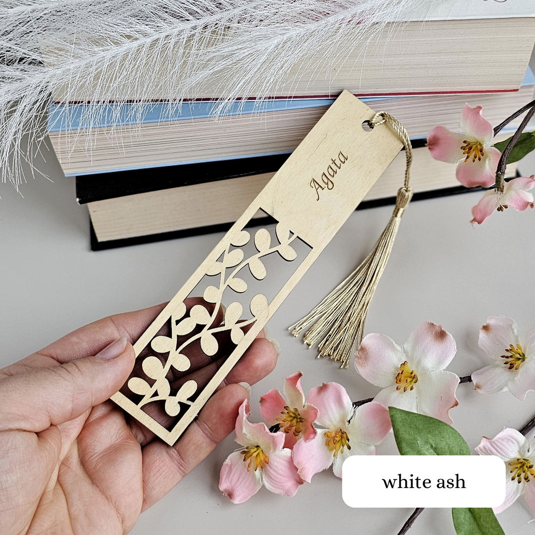 a hand holding a wooden bookmark with a tassel