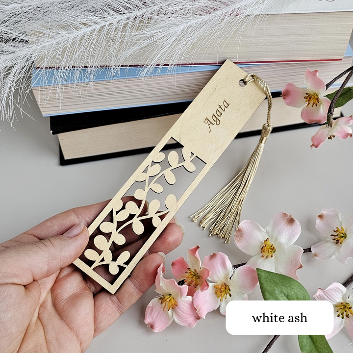 a hand holding a wooden bookmark with a tassel