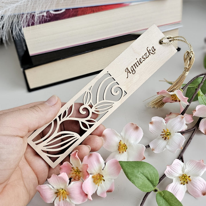 a person holding a bookmark next to some flowers