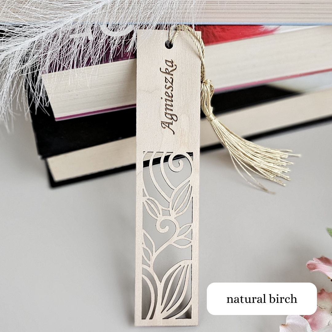 A wooden bookmark with a decorative cutout design, attached to a tassel, is placed on top of a stack of books.