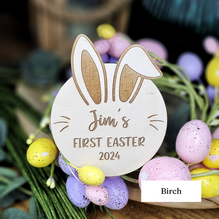 A wooden sign with a bunny ear design and the text "Jim's FIRST EASTER 2023" is surrounded by Easter eggs in various colors.