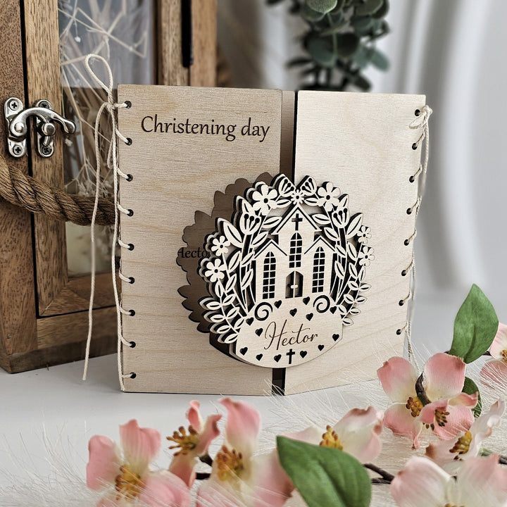A wooden card with a decorative wreath and the name "Hector" on it, placed on a table with pink flowers.