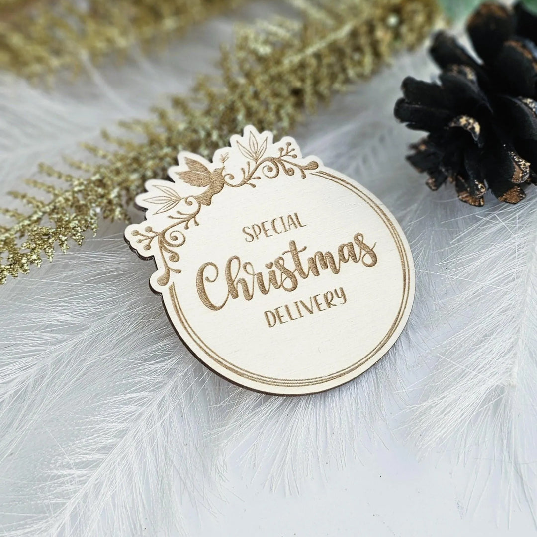 A wooden Christmas delivery label with the text "Special Christmas Delivery" is placed on a white surface, surrounded by decorative elements such as feathers and pine cones.