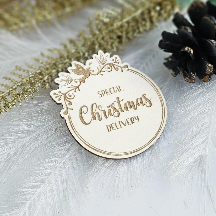 A wooden Christmas delivery label with the text "Special Christmas Delivery" is placed on a white surface, surrounded by decorative elements such as feathers and pine cones.