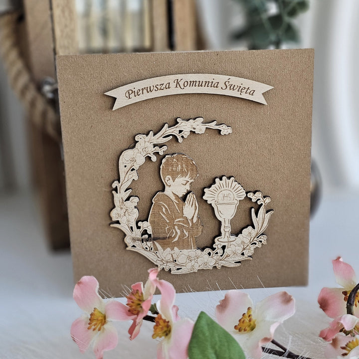 a wooden card with a carved image of a boy praying, surrounded by a wreath and flowers.
