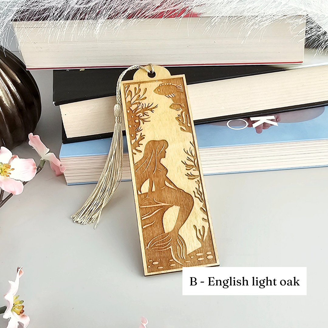A wooden mermaid-themed bookmark with a tassel attached, placed on top of a stack of books.