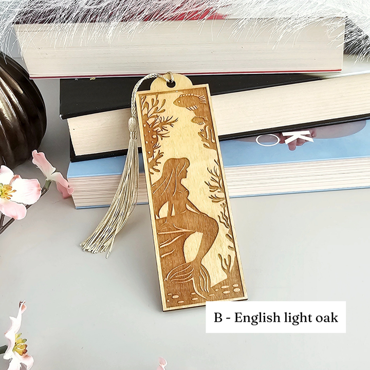 A wooden mermaid-themed bookmark with a tassel attached, placed on top of a stack of books.
