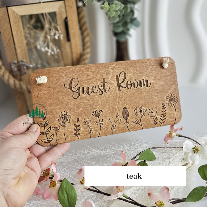 A wooden sign with the word "Guest Room" written on it, surrounded by various floral designs.