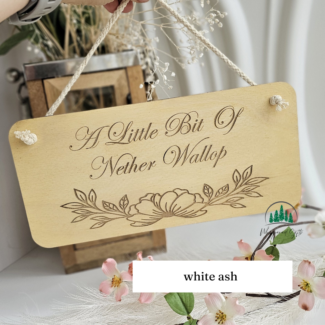 A wooden sign with the text "A Little Bit Of Neither Wallop" is hanging from a rope, surrounded by flowers and greenery.