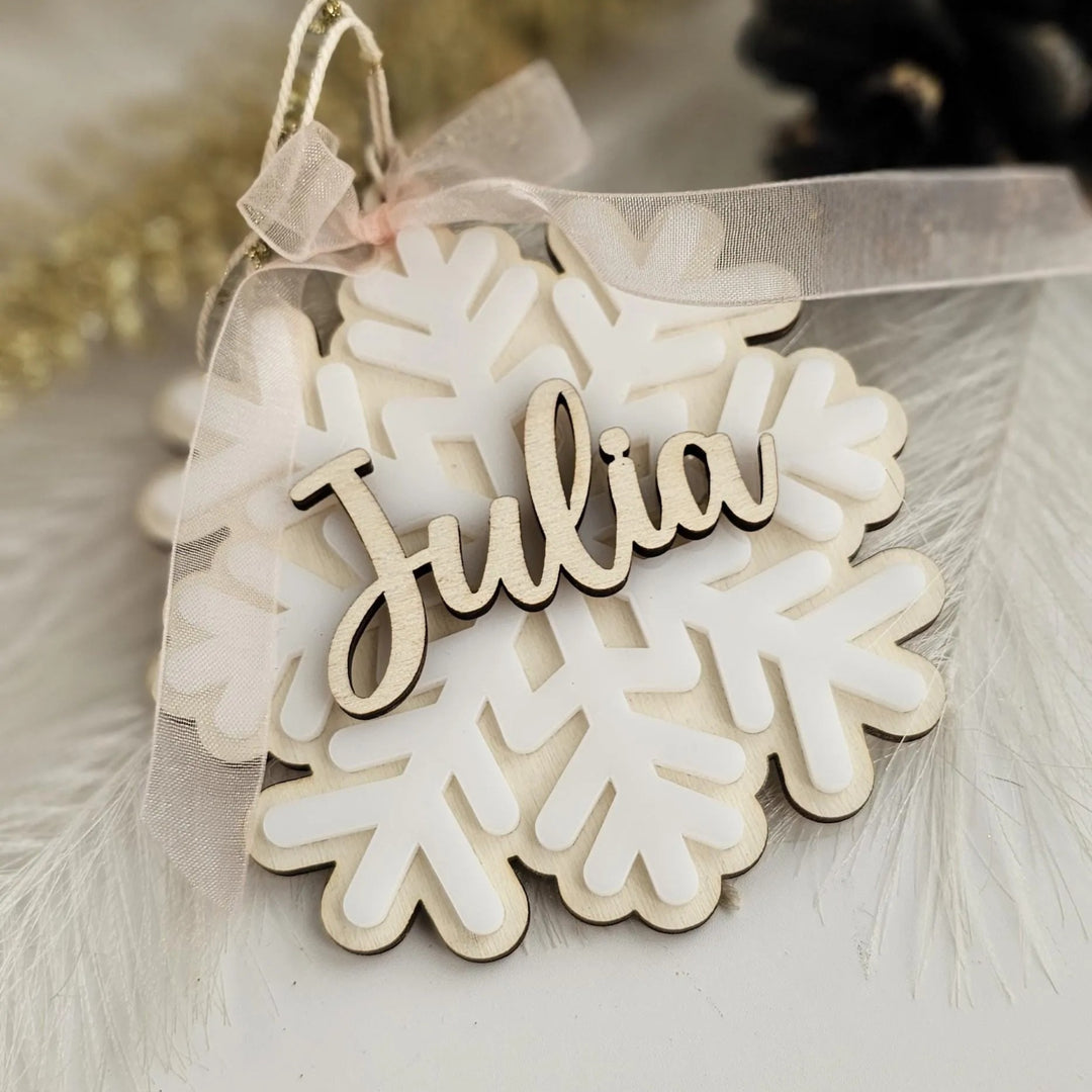 A wooden snowflake ornament with the name "Julia" written on it, tied with a ribbon.