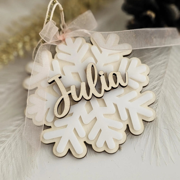 A wooden snowflake ornament with the name "Julia" written on it, tied with a ribbon.