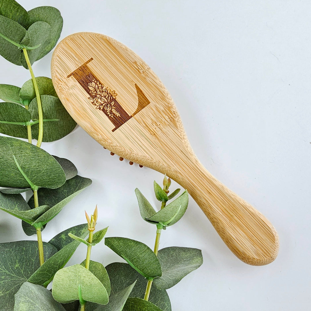 A wooden brush with a decorative design on it, placed on a white surface next to some green leaves.