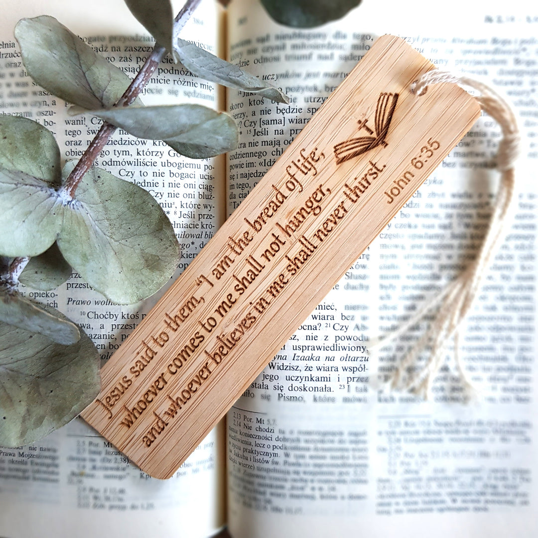 A wooden bookmark with a Bible verse engraved on it, resting on top of an open book with text visible.