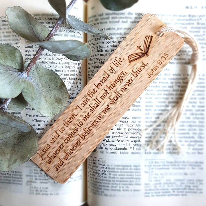 A wooden bookmark with a Bible verse engraved on it, resting on top of an open book with text visible.