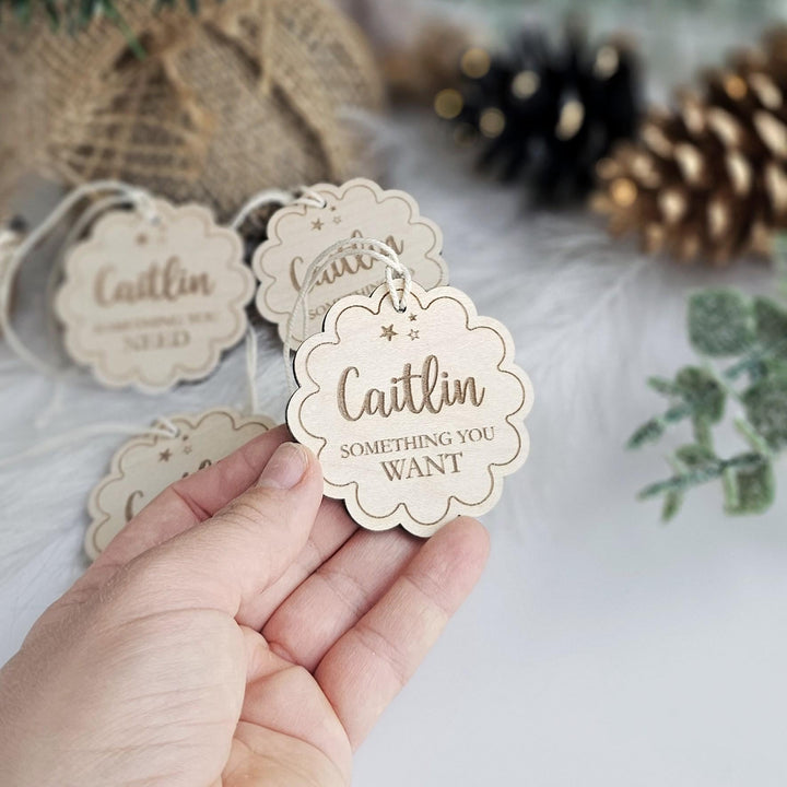 A hand holding a wooden tag with the name "Caitlin" and the phrase "Something you want" printed on it.