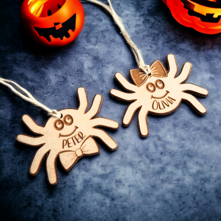 two wooden spider ornaments with names on them, placed on a dark surface.