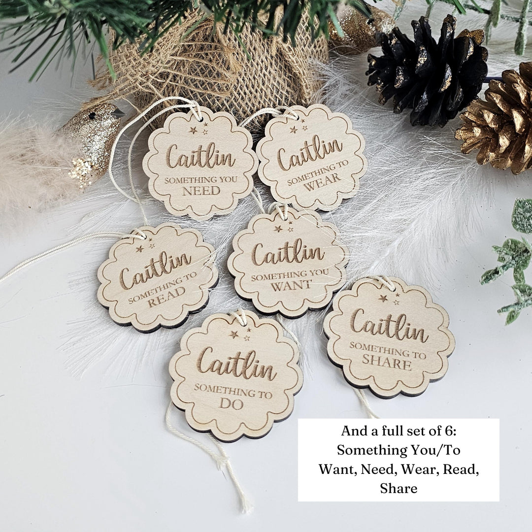 a set of six wooden tags with the name "Caitlin" written on them, placed on a white surface. The tags are arranged in a circular pattern, and there are pine cones and greenery in the background.