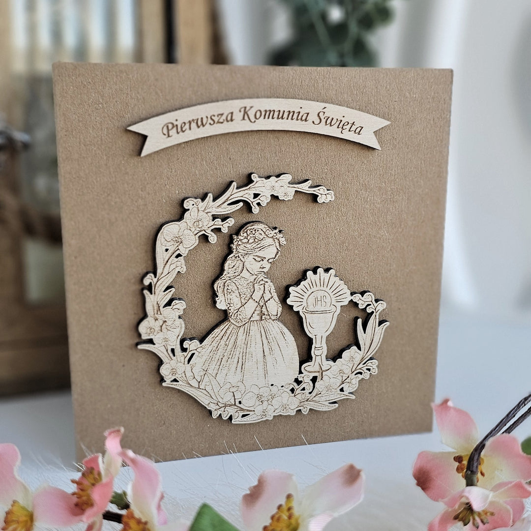 A wooden card with a carved image of a young girl praying, surrounded by flowers, and a banner that says "Pierwsza Komunia Swieta" (Praying Girl).