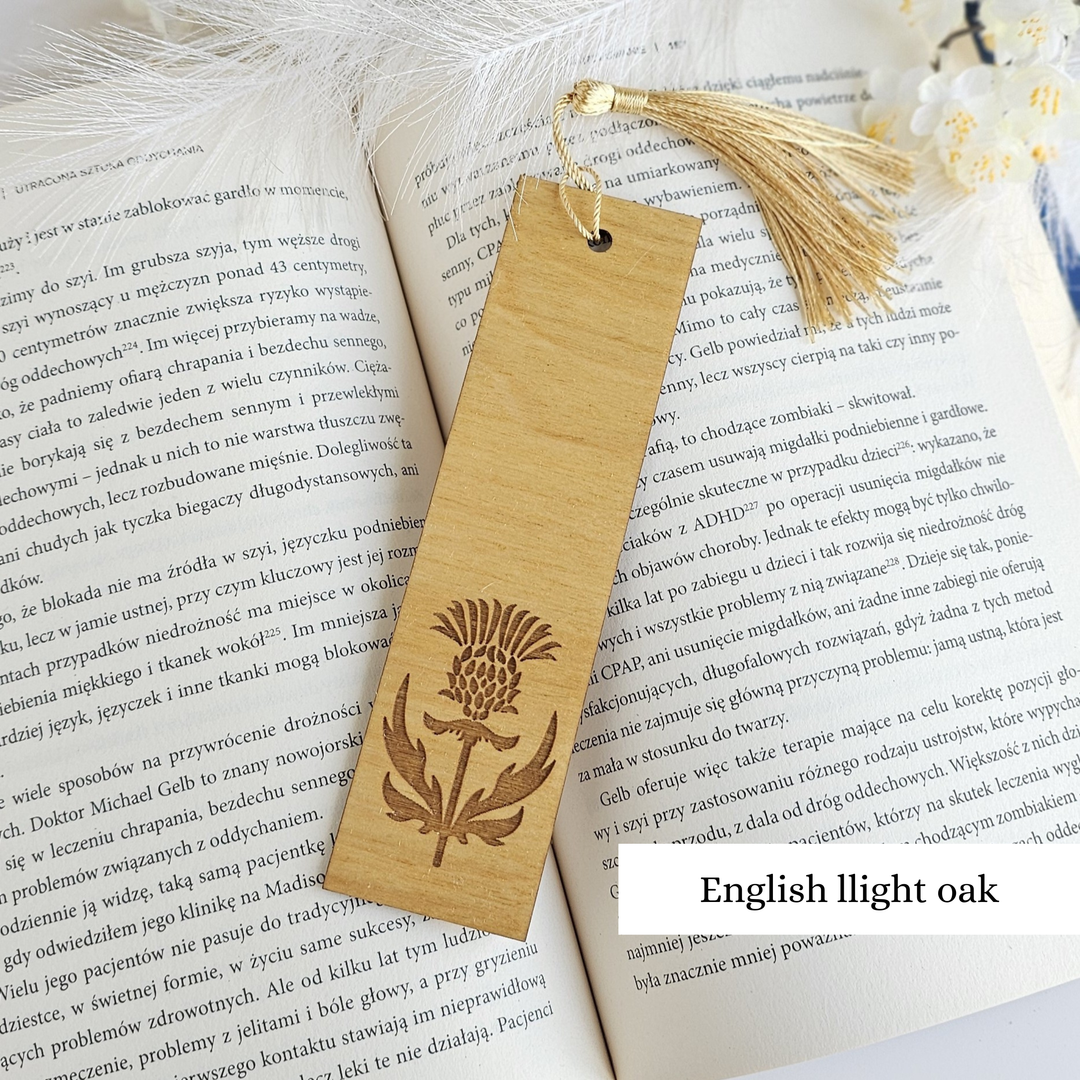 An open book with text in Polish, featuring a wooden bookmark with a design of a thistle flower.